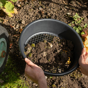 Person holding a black garden riddle and using it to filter soil against a natural background