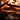 Wood being cooked in a pizza oven with pizzas inside, featuring the brand logo.
