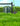 Green watering can, garden kneeler, and garden lawn edger on grass with a blue sky background